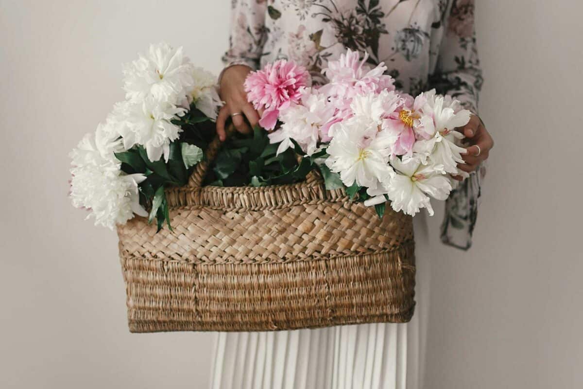 A person holding a woven kete filled with pink and white flowers