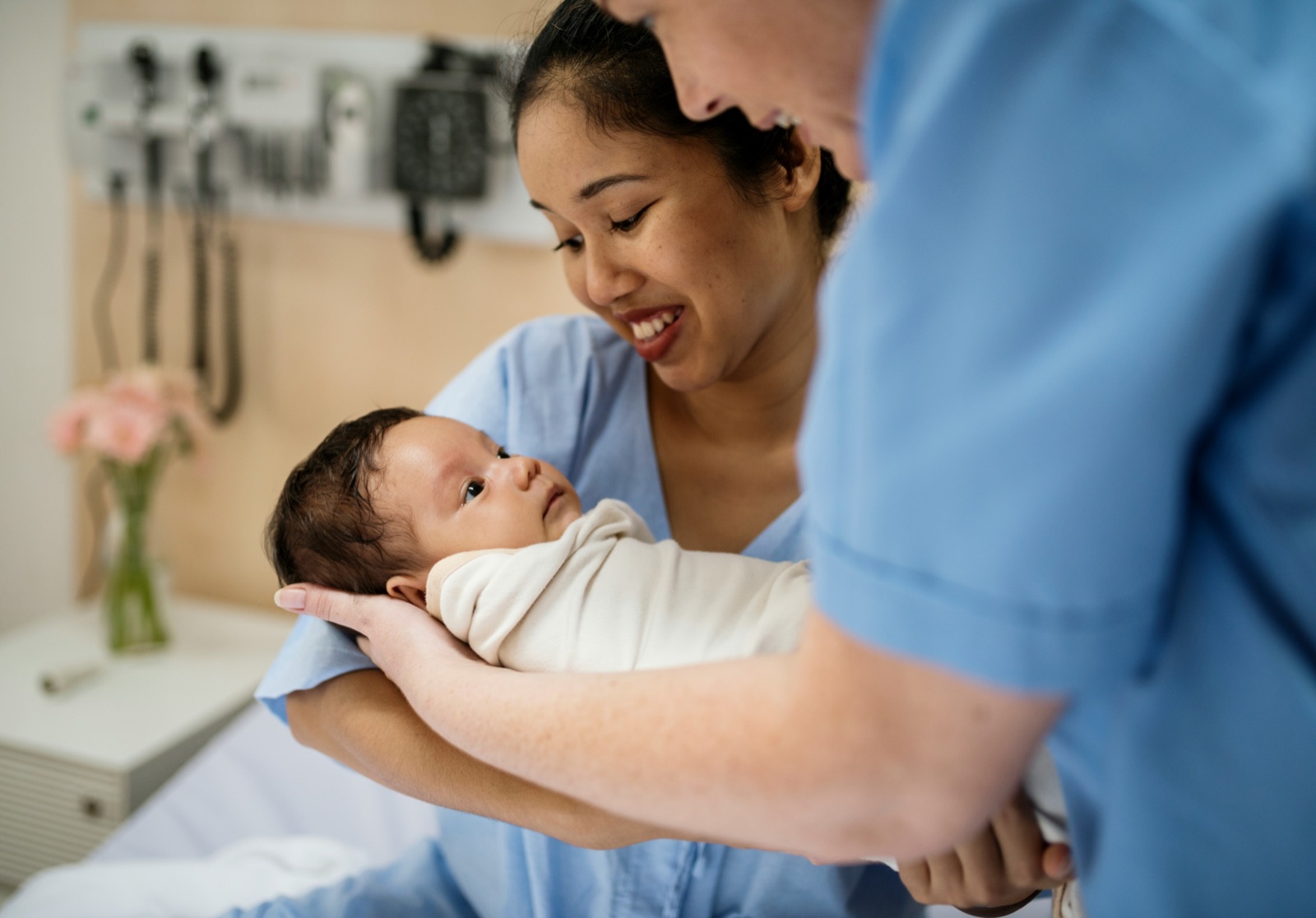 A nurse holding a newborn with the mother looking on