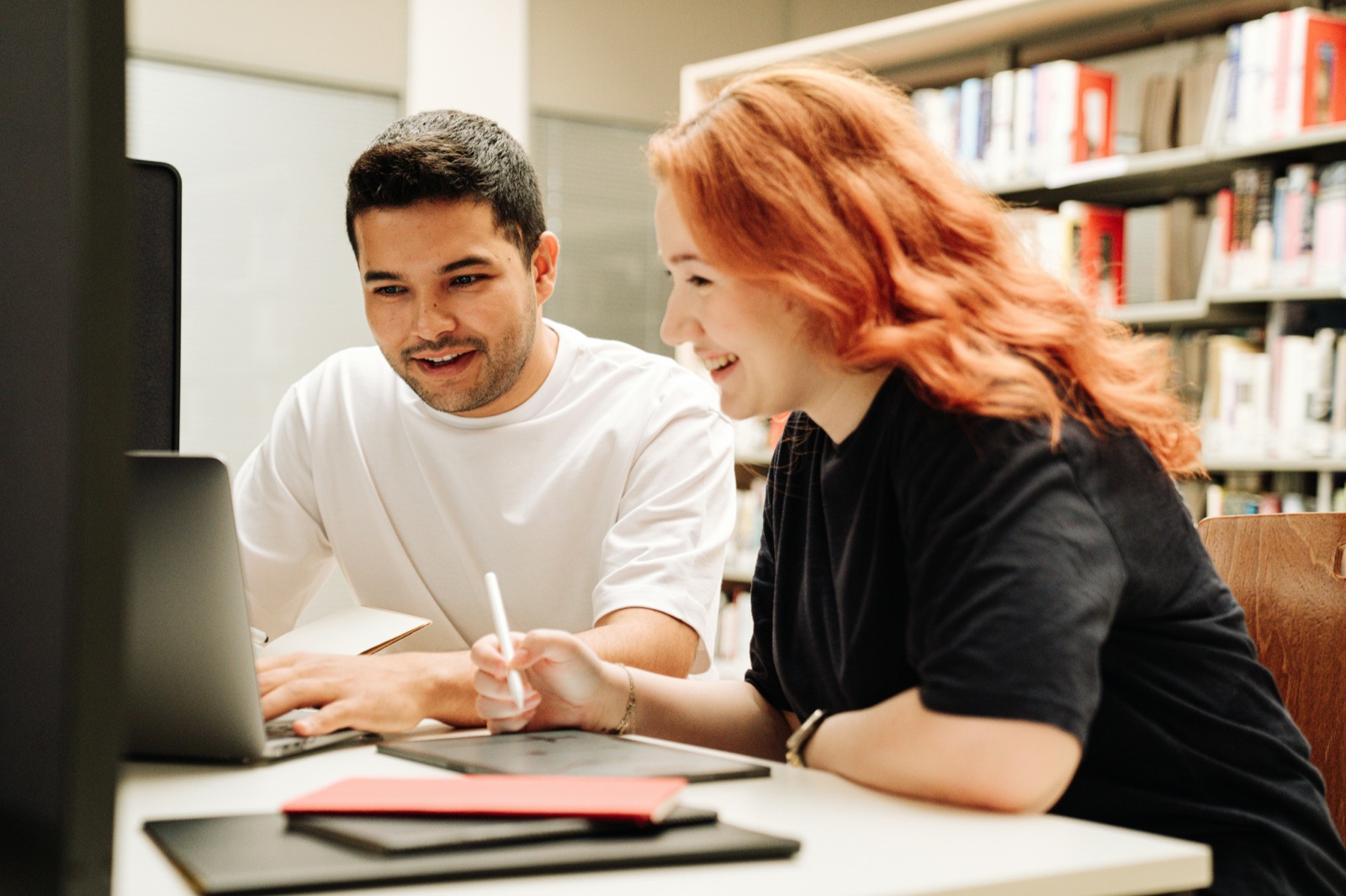 Two people talking over a laptop in a library